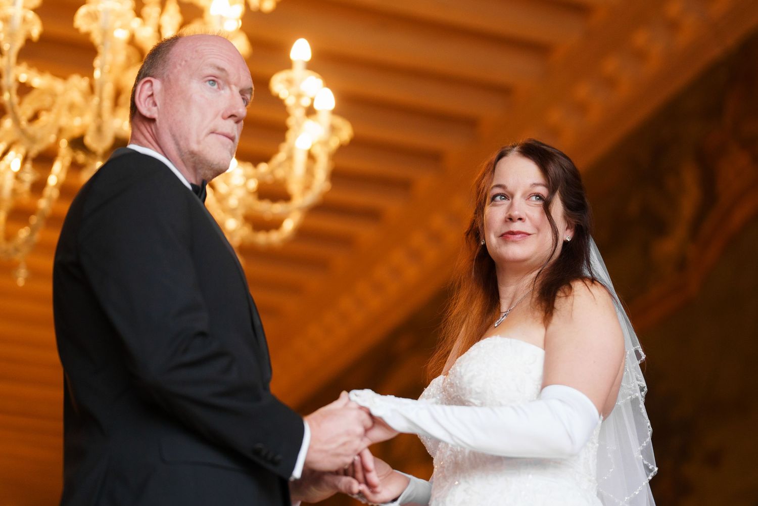 A couple shares their first dance at an elegant wedding reception in a golden-lit ballroom.