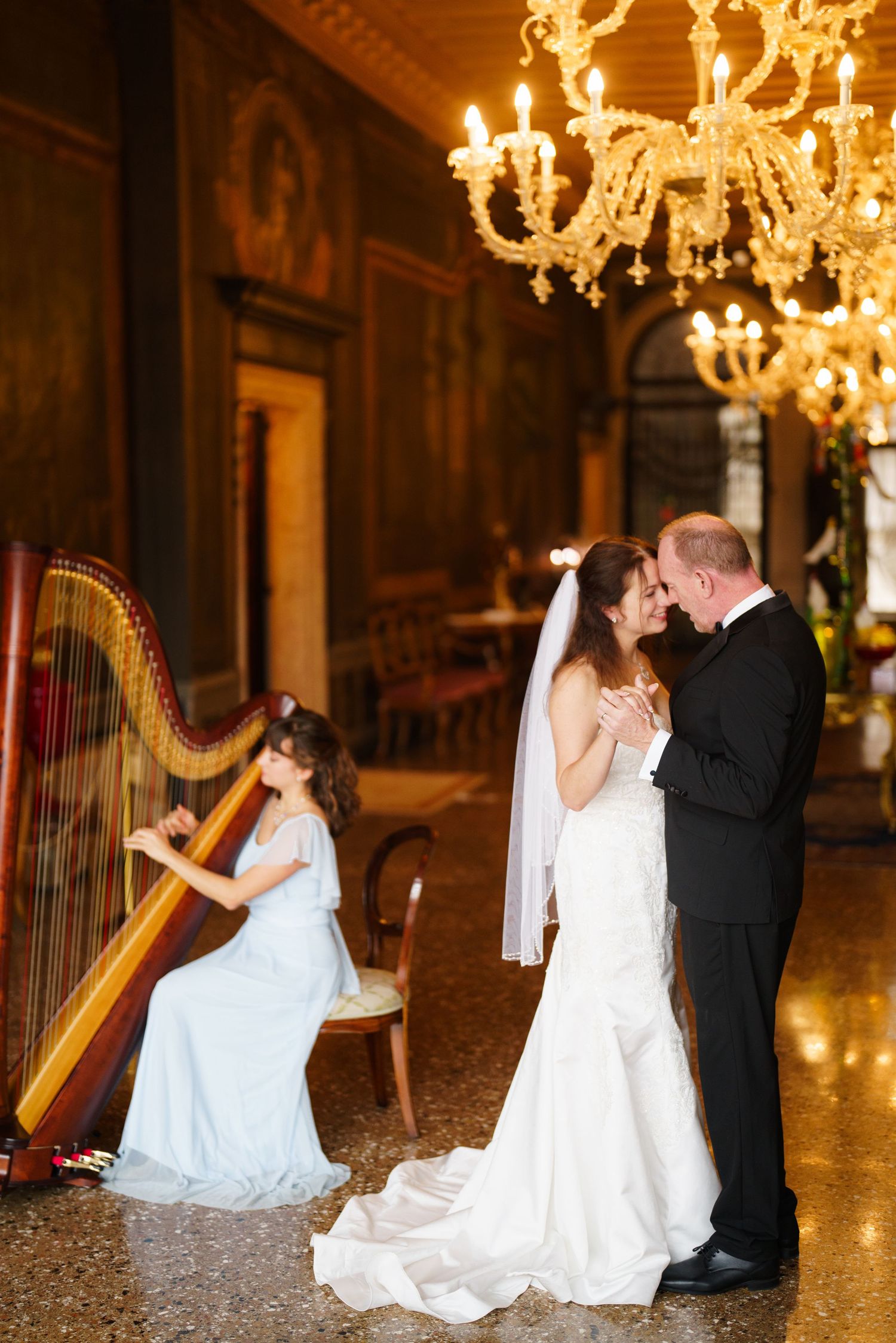 Elegant wedding ceremony in ornate ballroom with crystal chandelier and harpist performing in white gown.