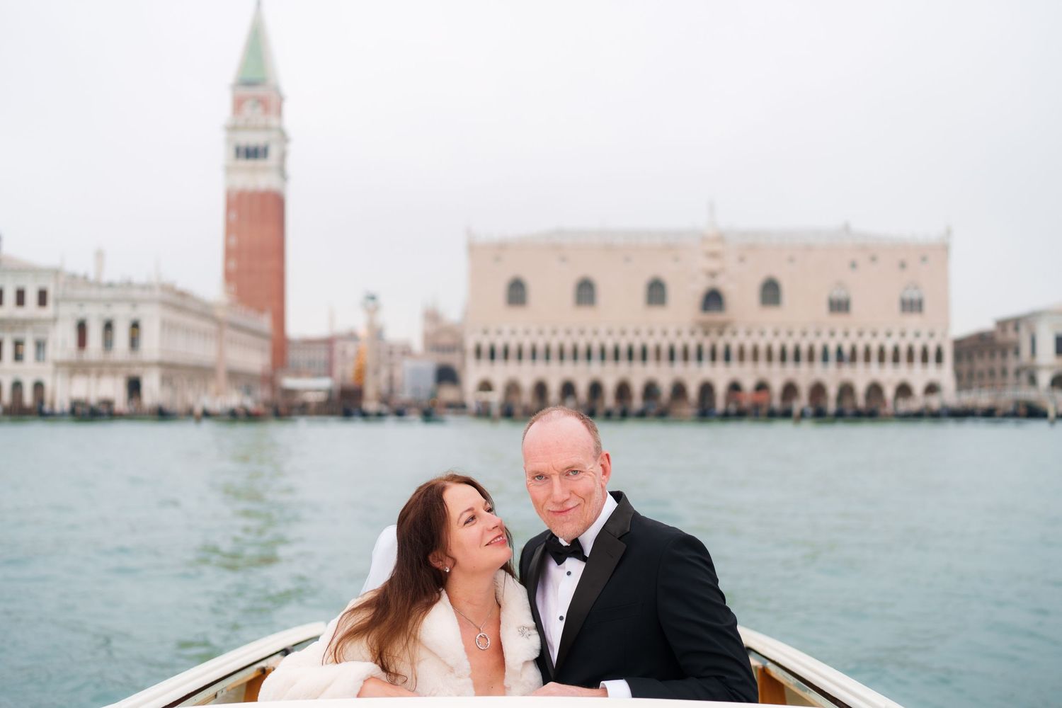 A couple shares a romantic moment on a boat in Venice with the Doge's Palace and St. Mark's Campanile in the background.