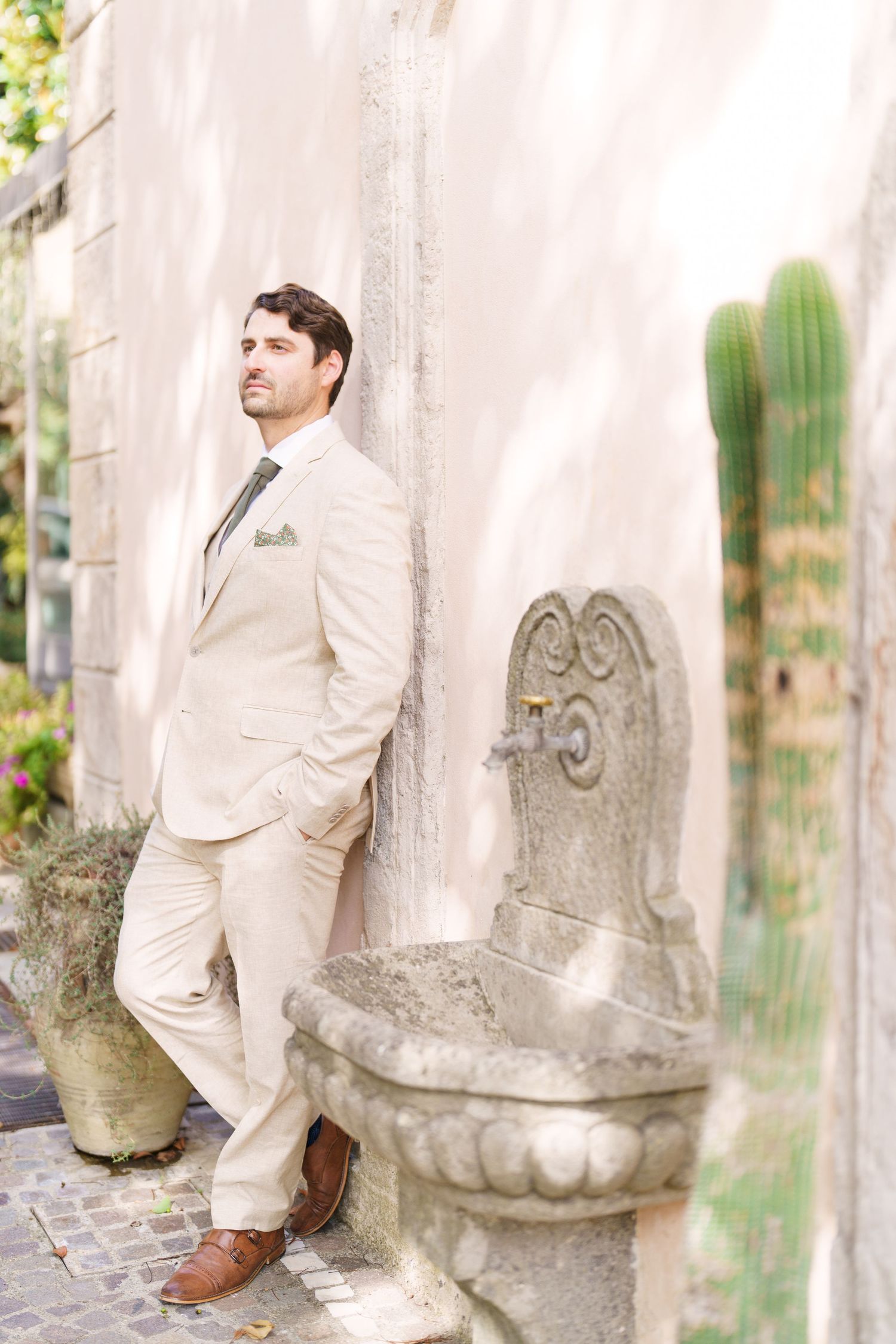Formal portrait against stone fountain wearing cream colored suit.