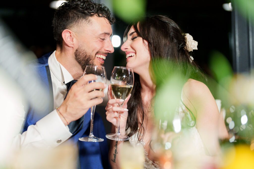 Candid black and white photo of couple sharing champagne and laughter at reception.