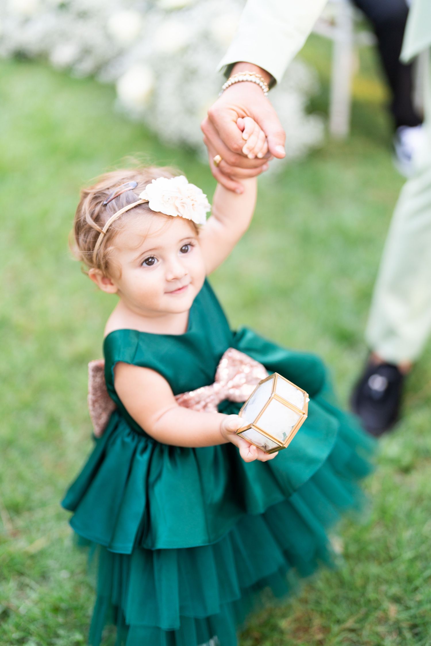 Small child in emerald green dress plays on grass during wedding celebration.