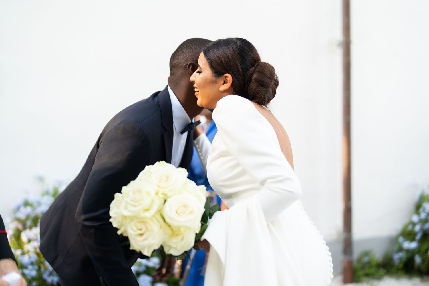 A romantic wedding moment with a couple sharing a kiss while holding a bouquet of white roses.