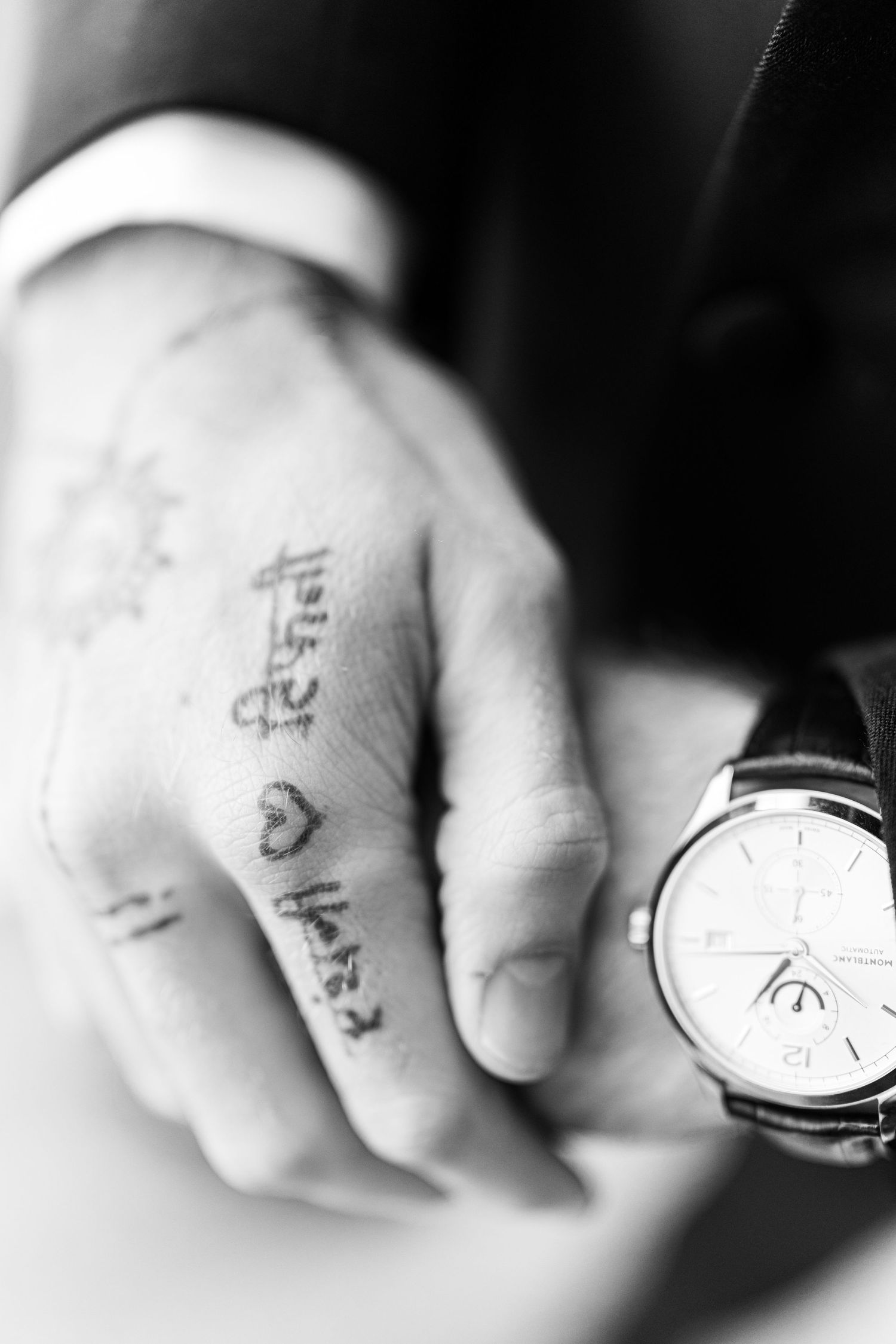 Close-up black and white shot of hands wearing a watch with temporary tattoos visible.