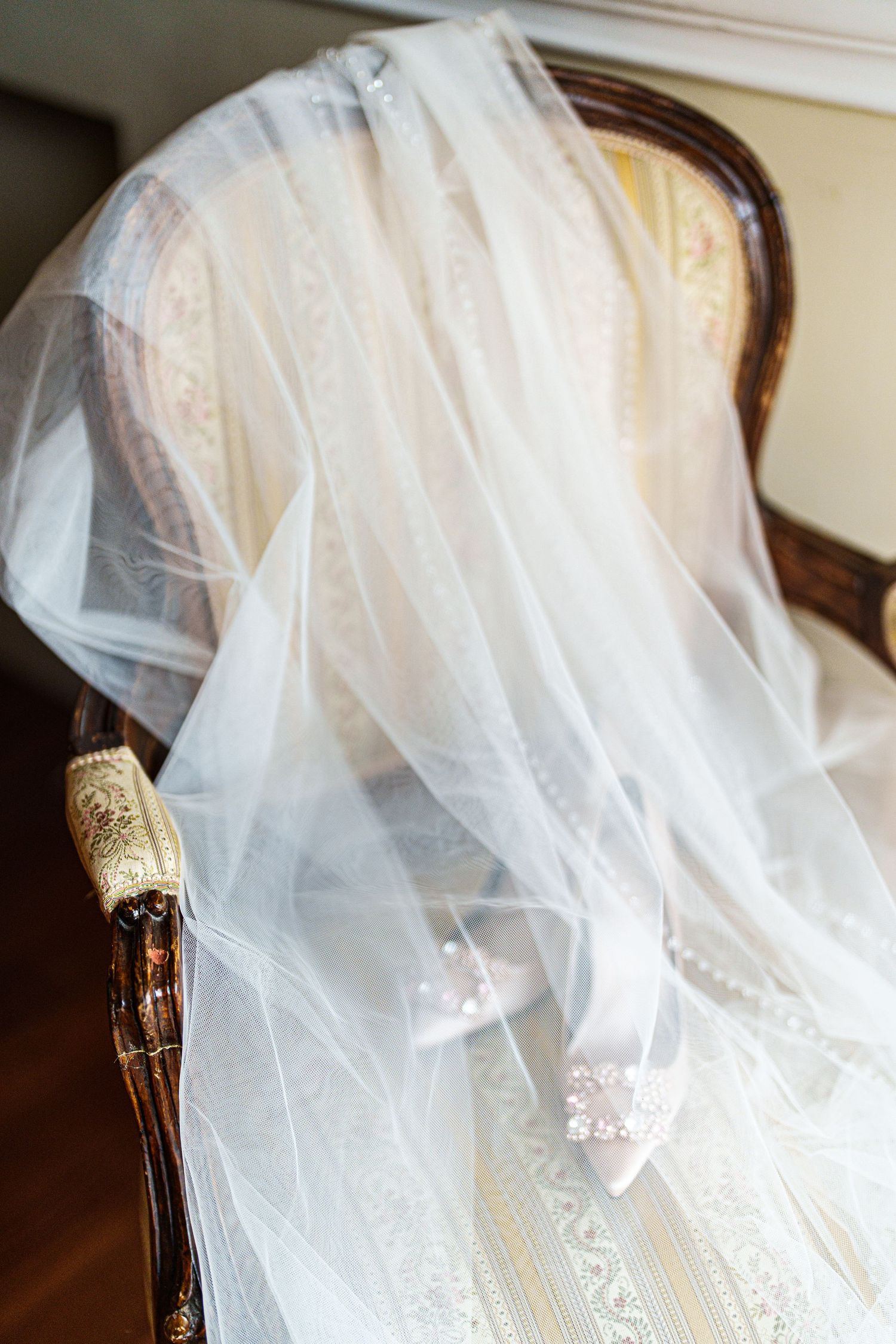 Delicate white wedding veil draped elegantly with champagne bottle in background.