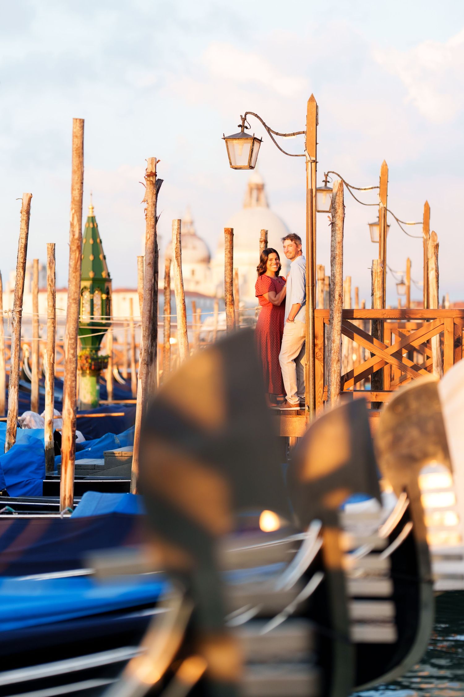 Romantic couple embracing on Venice gondola dock at sunset, with Santa Maria della Salute in the background.