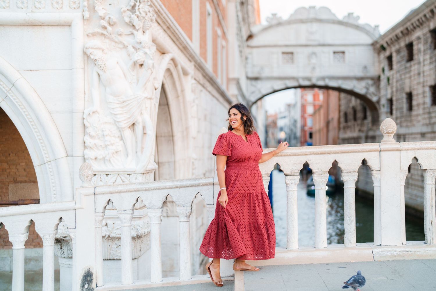 Woman in red dress posing near ornate white bridge in Venice, Italy with canal in background.
