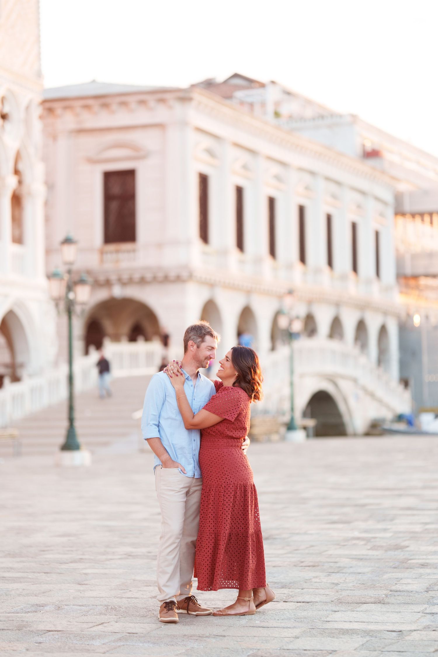Couple embracing and smiling at each other in Piazza San Marco, Venice, with the Doge's Palace in the background.