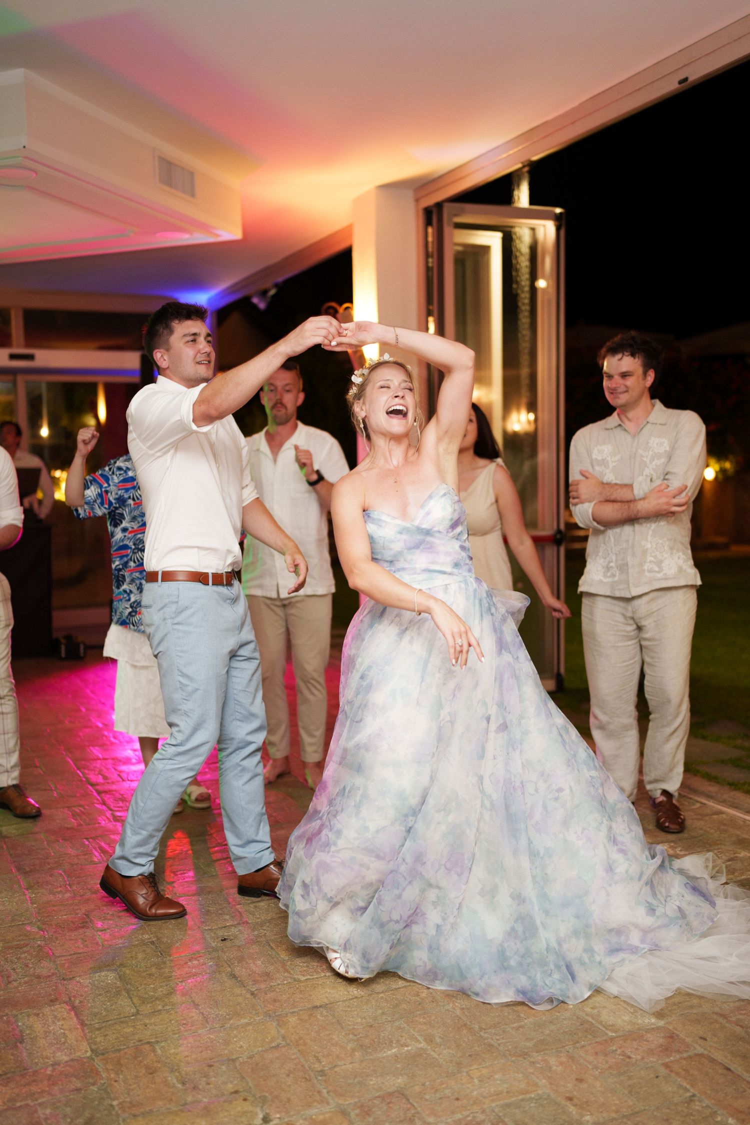 Bride in floral gown dancing joyfully with guests at an elegant outdoor wedding reception.