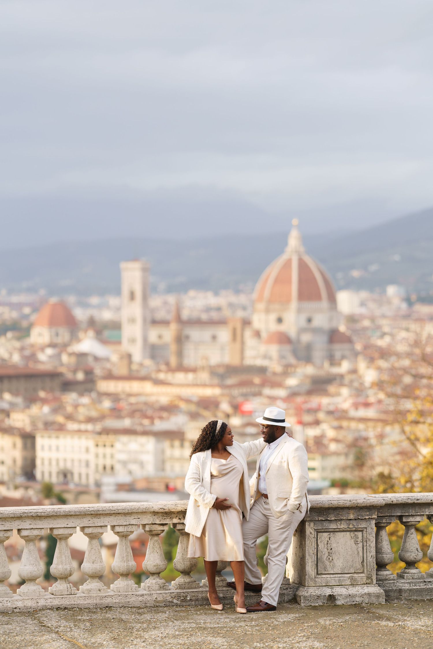 Couple in white outfits standing on a terrace overlooking Florence skyline with the Duomo cathedral in background.