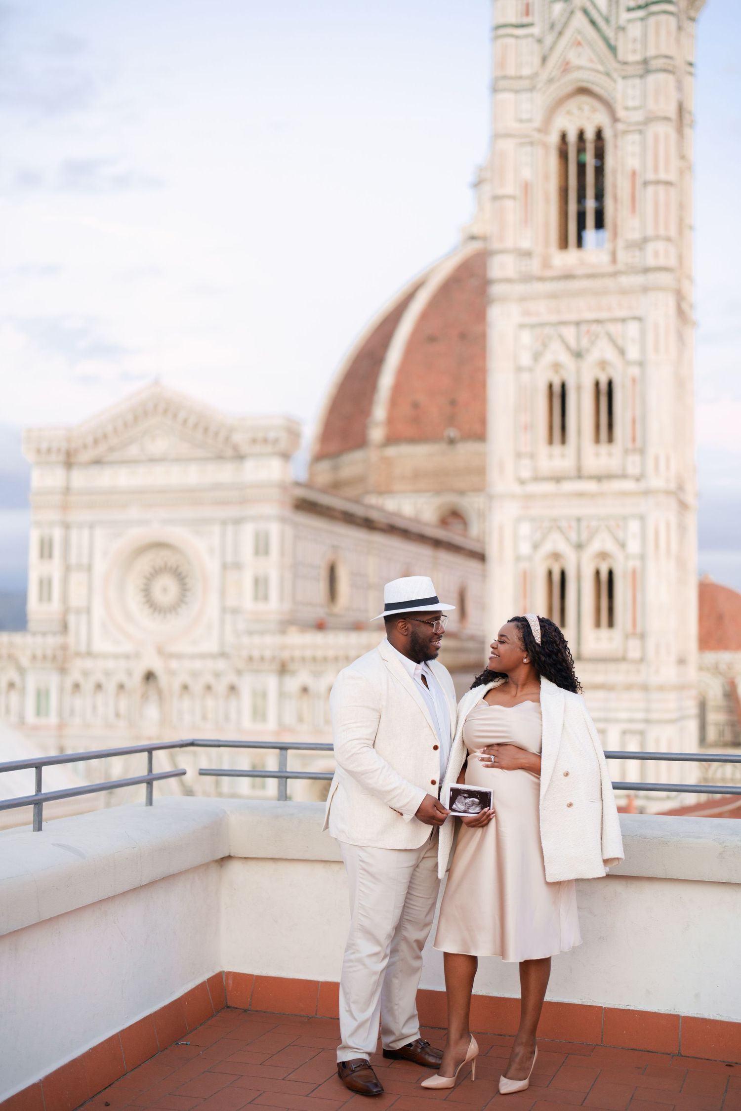 Couple holding ultrasound photo on rooftop terrace with Florence Cathedral dome backdrop.