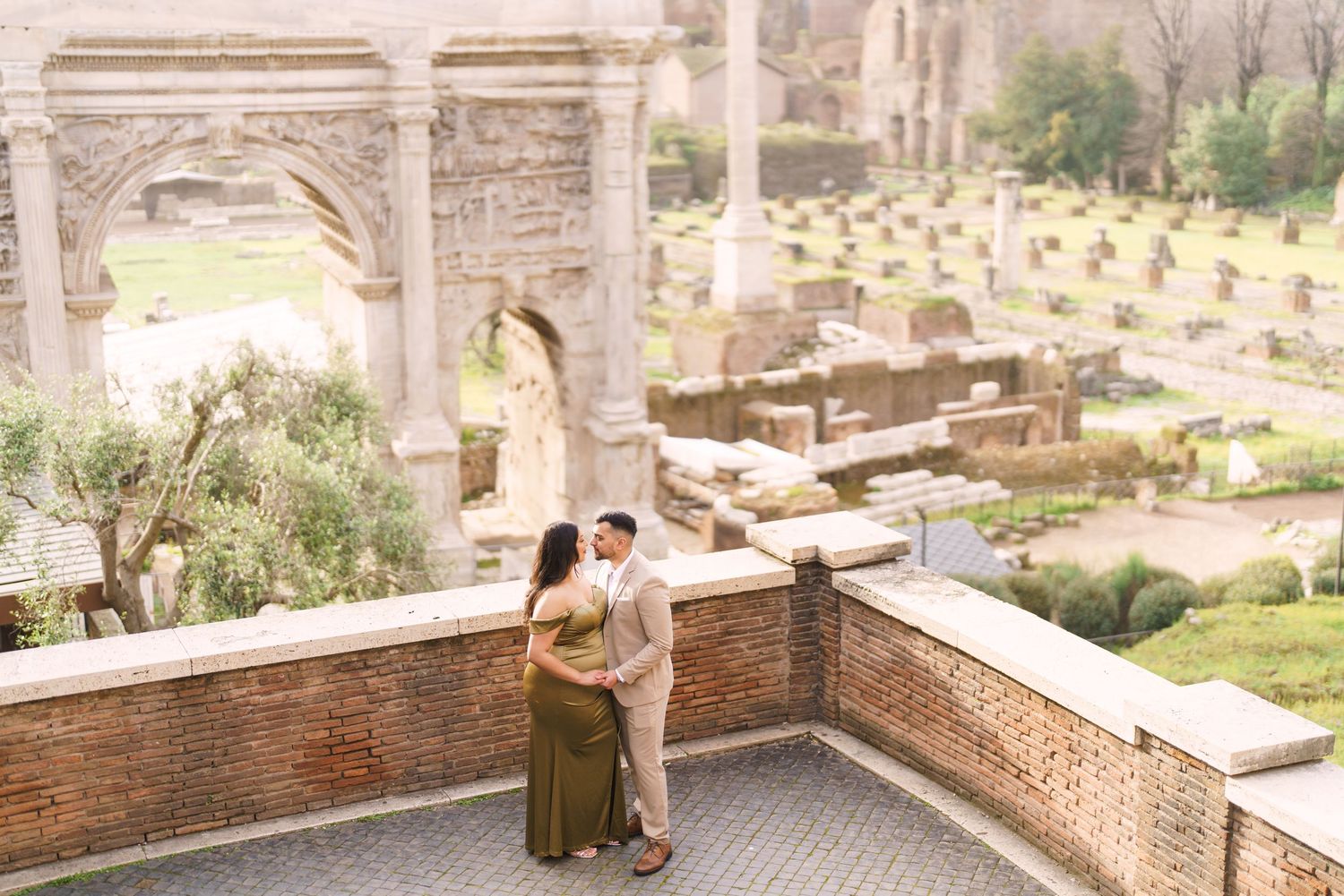 Couple embracing on a terrace overlooking ancient Roman ruins and lush greenery in Rome, Italy.