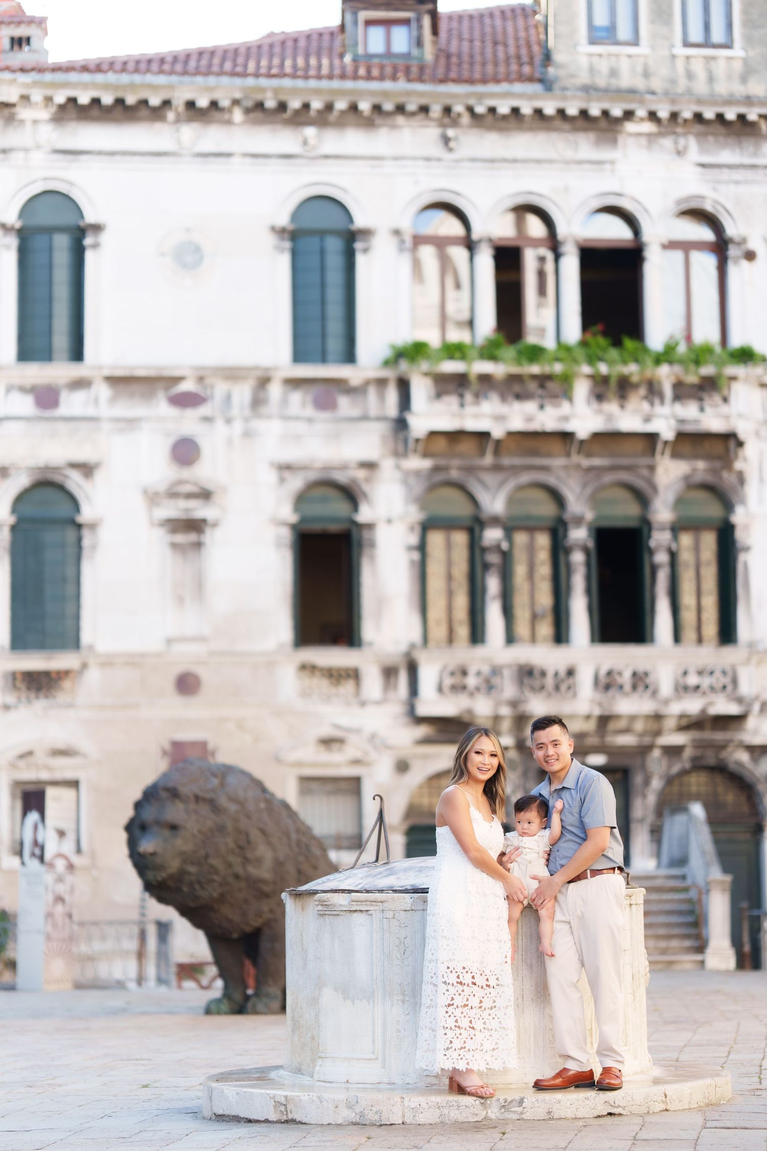Family of three posing by a stone well in a Venice piazza with historic architecture in the background.