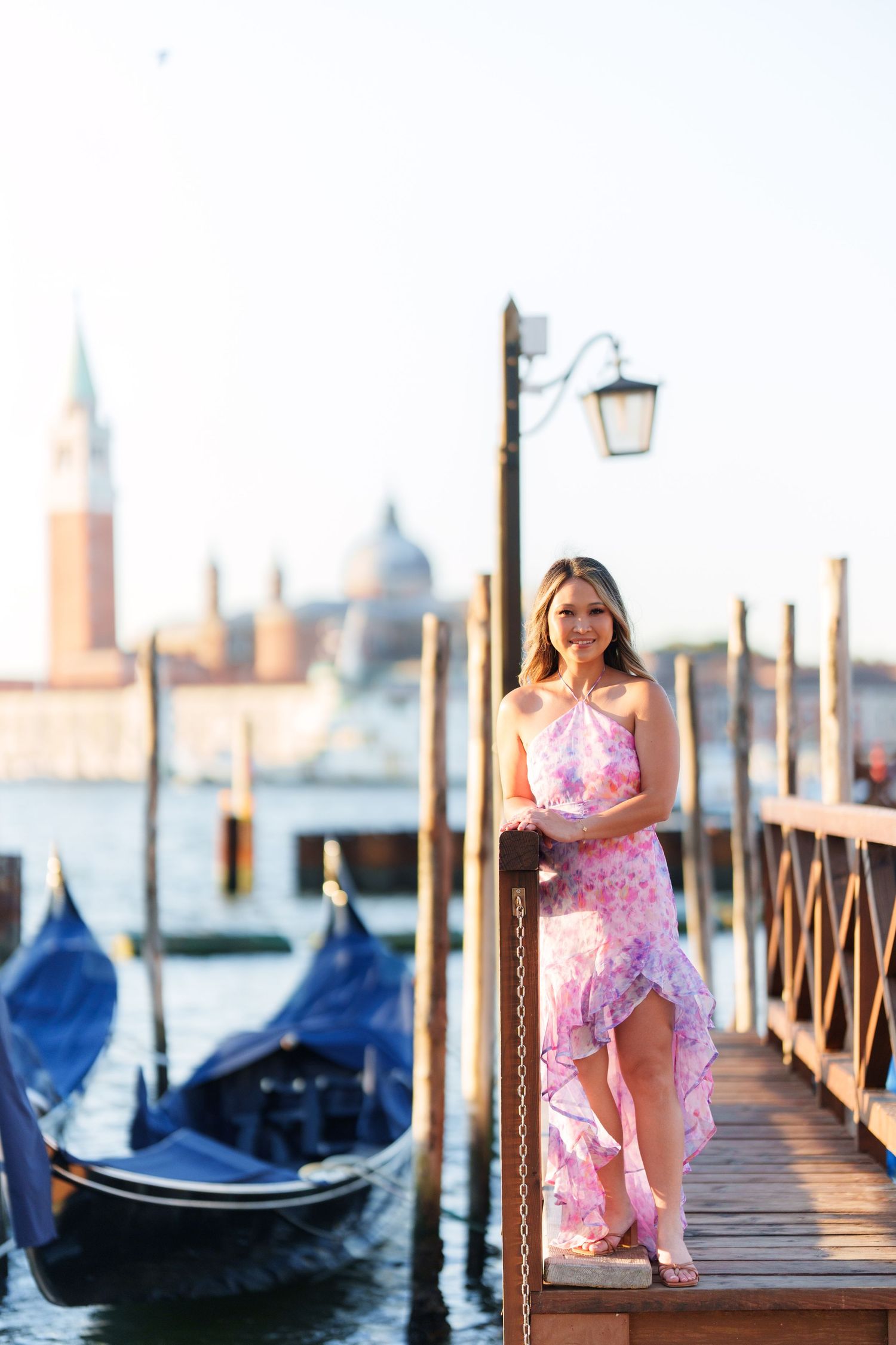 Woman in pink floral dress posing on Venice gondola dock with San Giorgio Maggiore church in background.