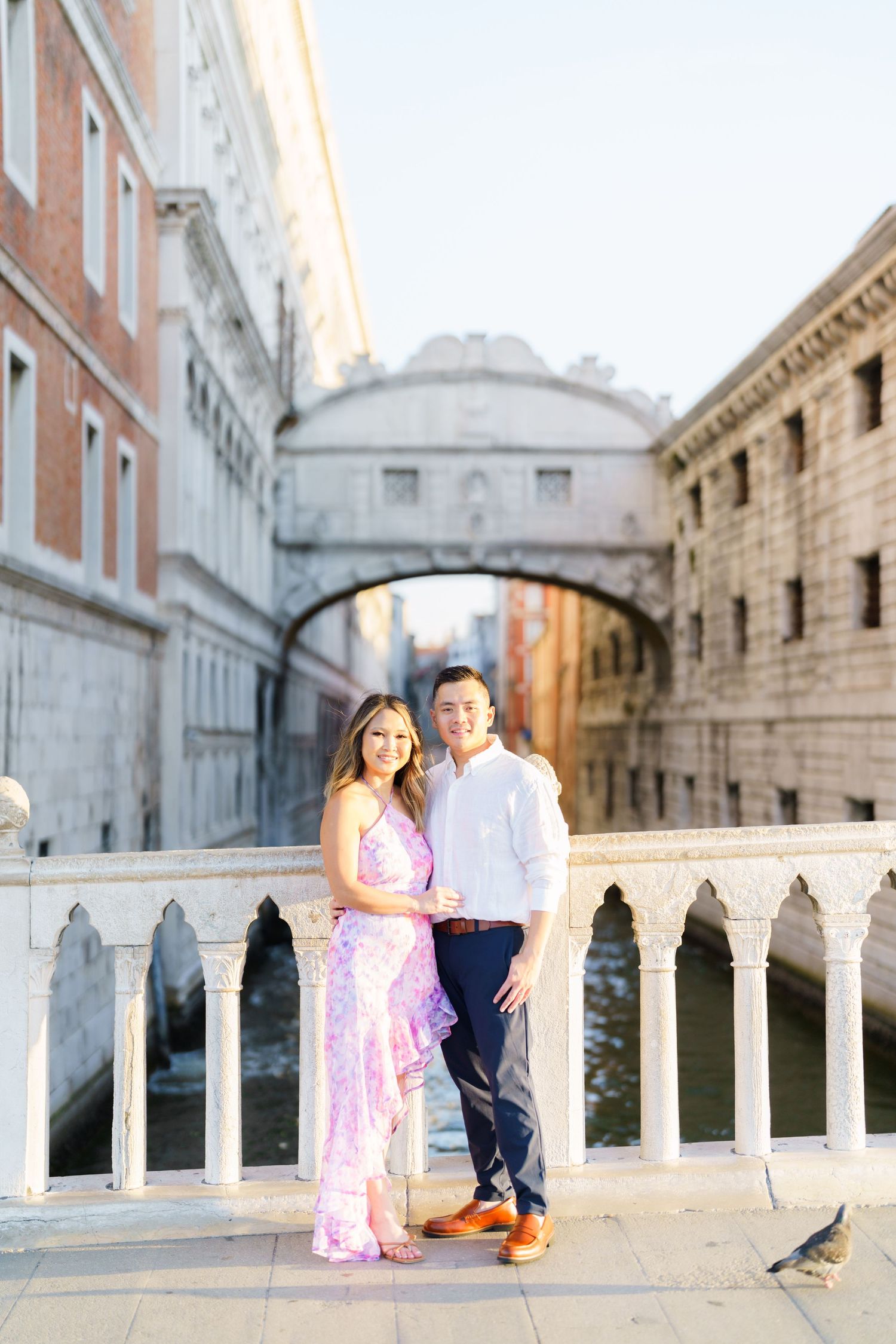Couple posing near the Bridge of Sighs in Venice, Italy, with marble columns and canal in background.