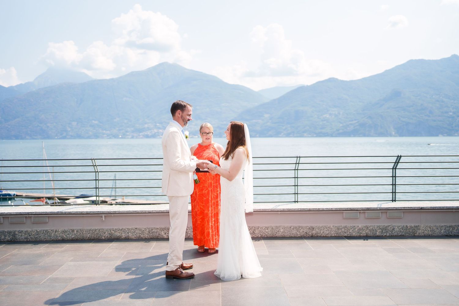 Couple exchanges wedding vows with officiant on lakeside terrace with mountain backdrop at Lake Como Italy.