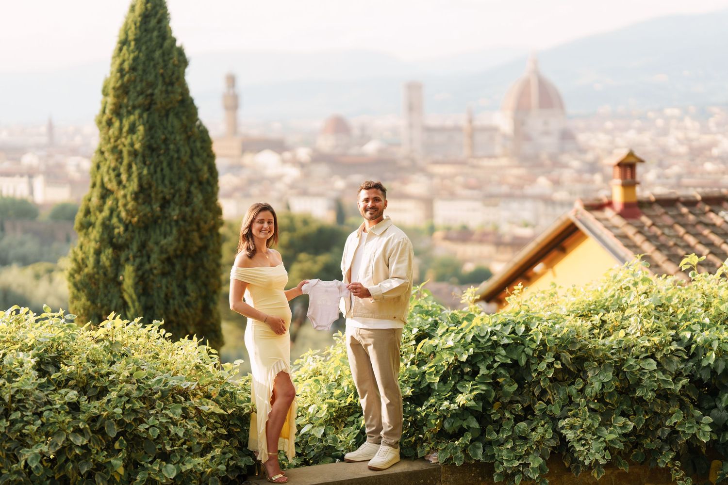 Couple posing with Florence skyline and Duomo cathedral backdrop in a lush garden setting.