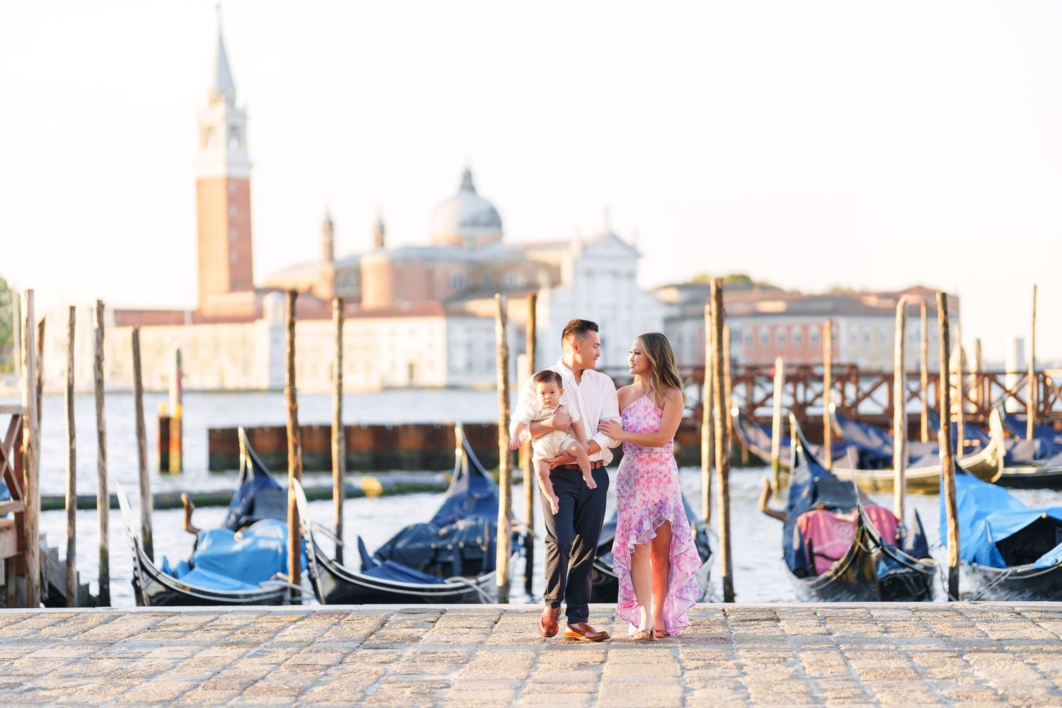 Family posing by Venice gondolas with San Giorgio Maggiore church in background on a sunny day.