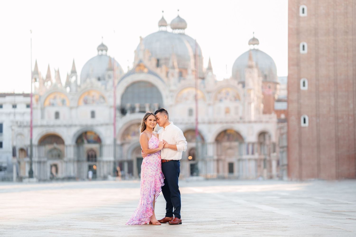 Couple embracing in St. Mark's Square, Venice, with the iconic Basilica di San Marco in the background at sunrise.