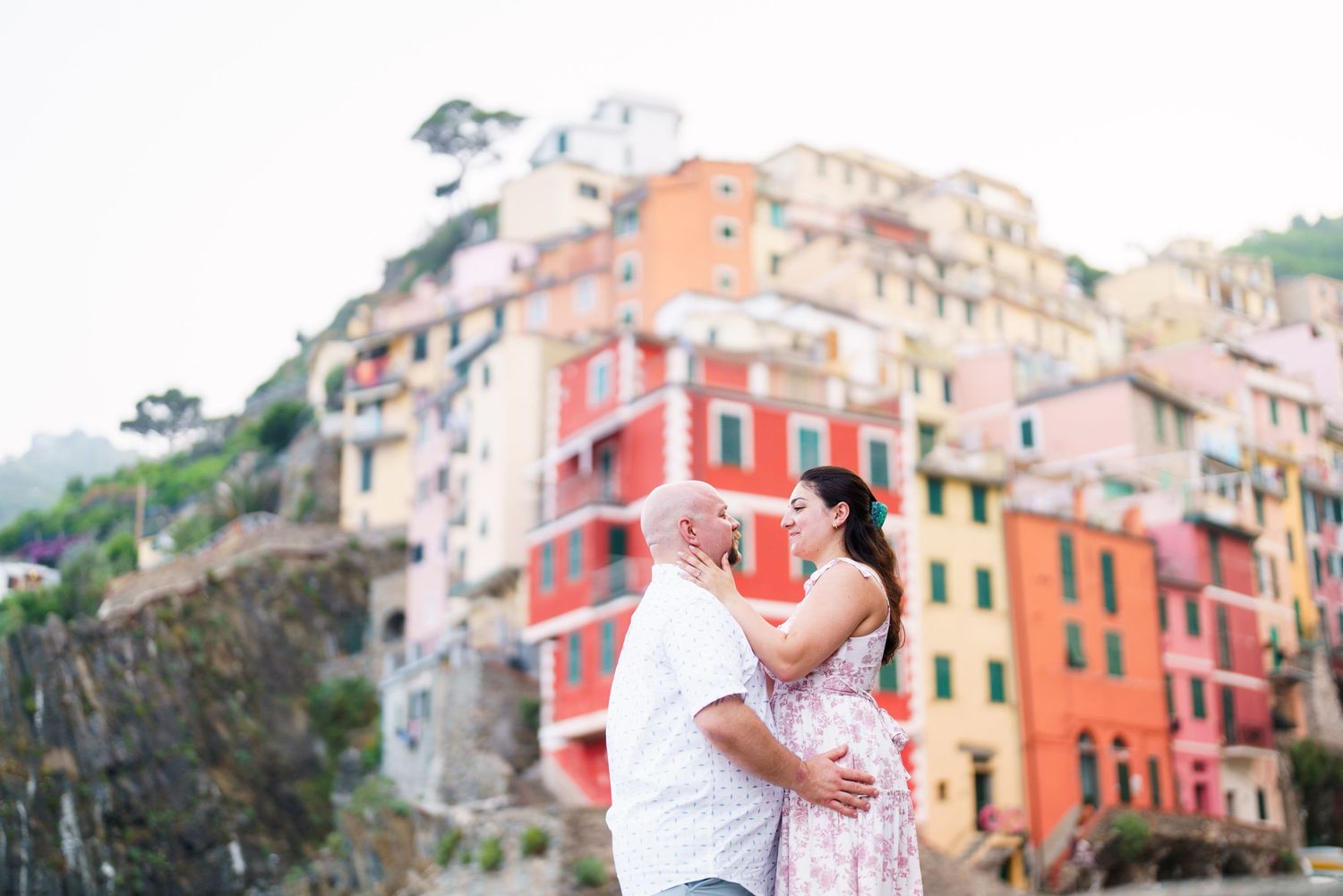 Couple embracing romantically in front of colorful buildings in Riomaggiore, Cinque Terre, Italy.