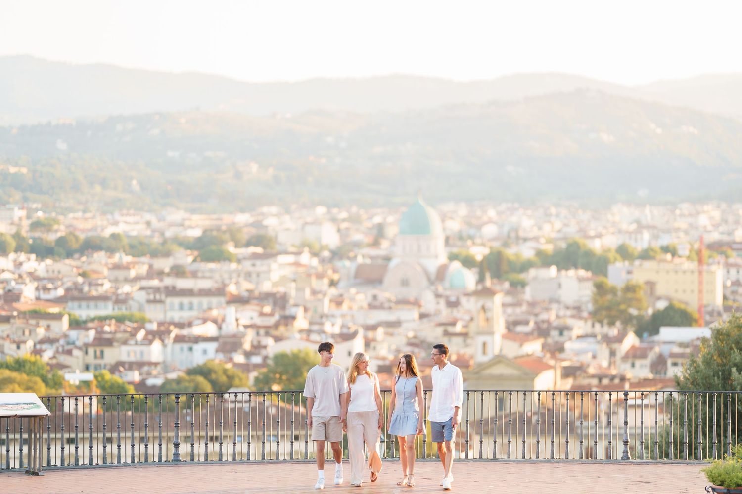 Family of four walking on a scenic overlook with Florence Italy cityscape and rolling hills in the background.