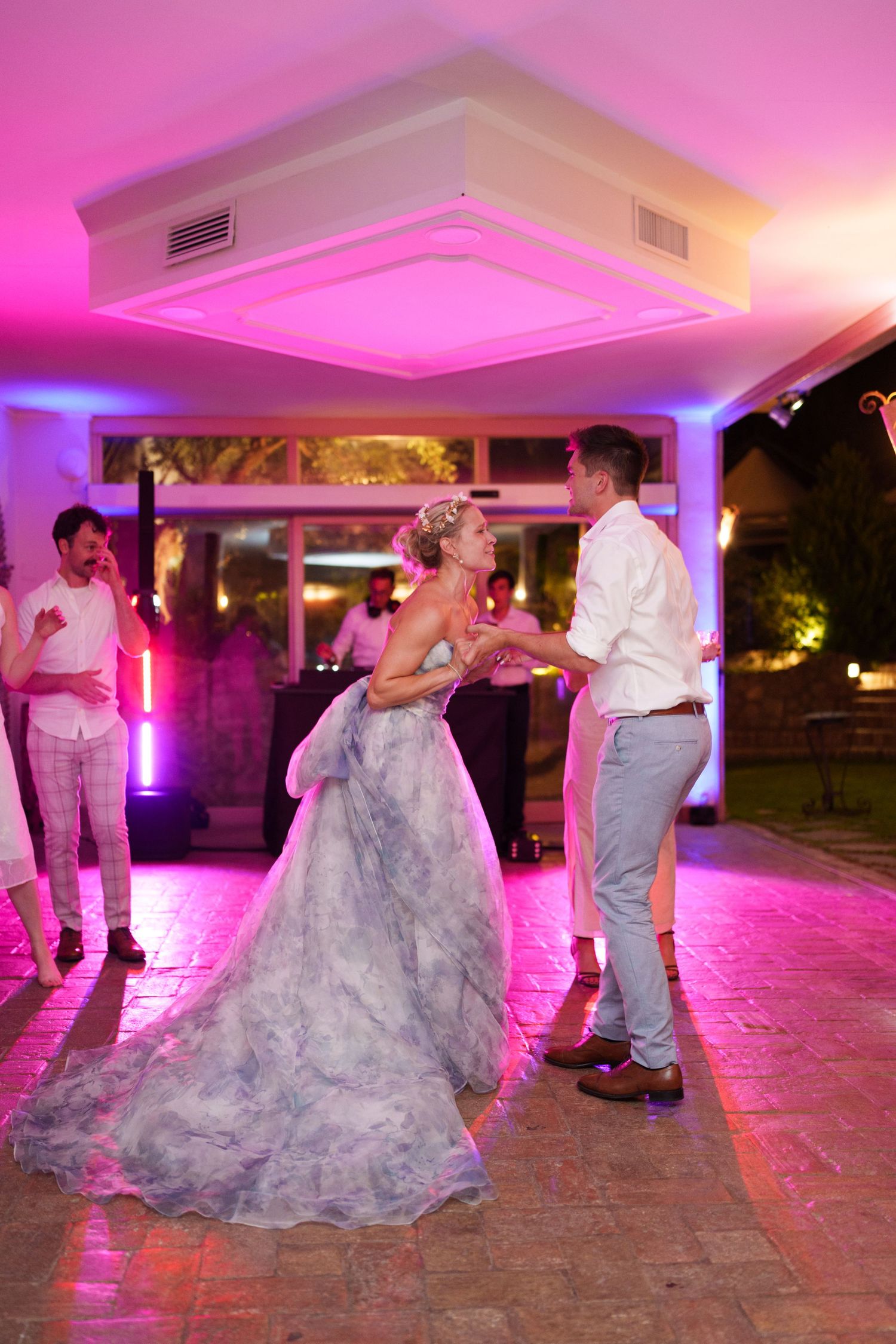 Bride and groom share their first dance under pink and blue lights at an elegant outdoor wedding reception.