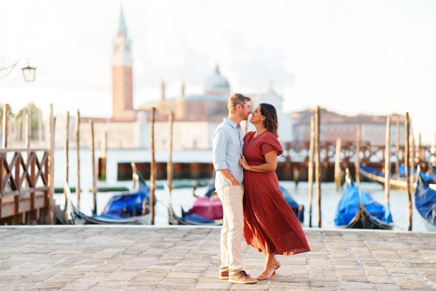 Couple sharing a romantic kiss on Venice waterfront with gondolas and San Giorgio Maggiore church in background.