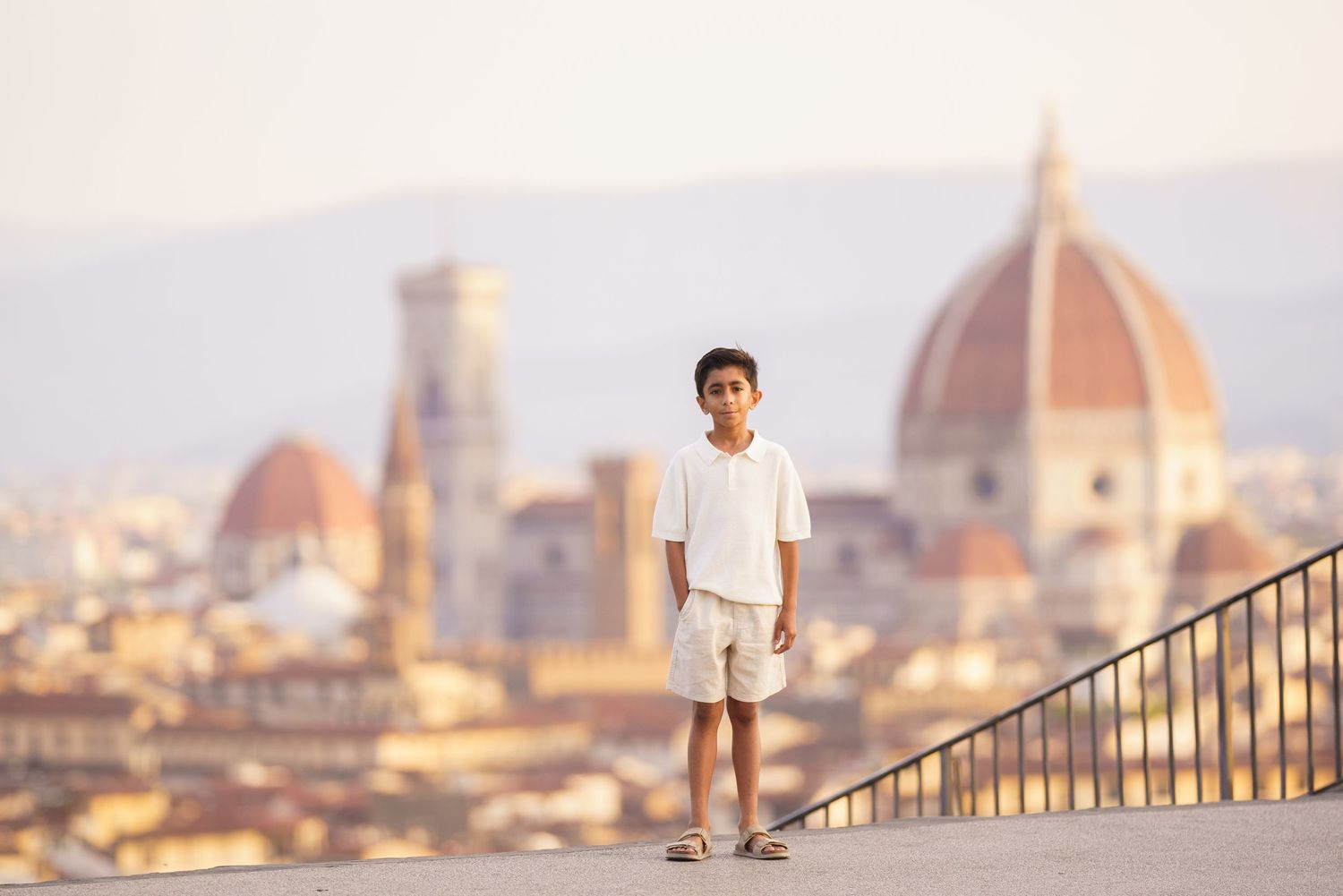 A young boy stands on a terrace overlooking Florence, Italy, with the iconic Duomo cathedral dome in the background.
