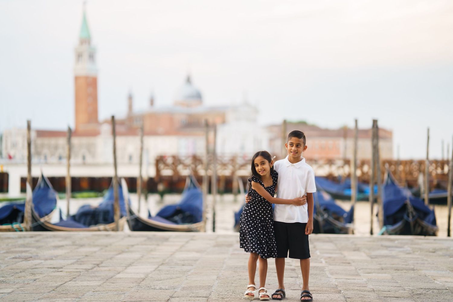 A couple poses on a Venice waterfront with gondolas and San Giorgio Maggiore church in the background.