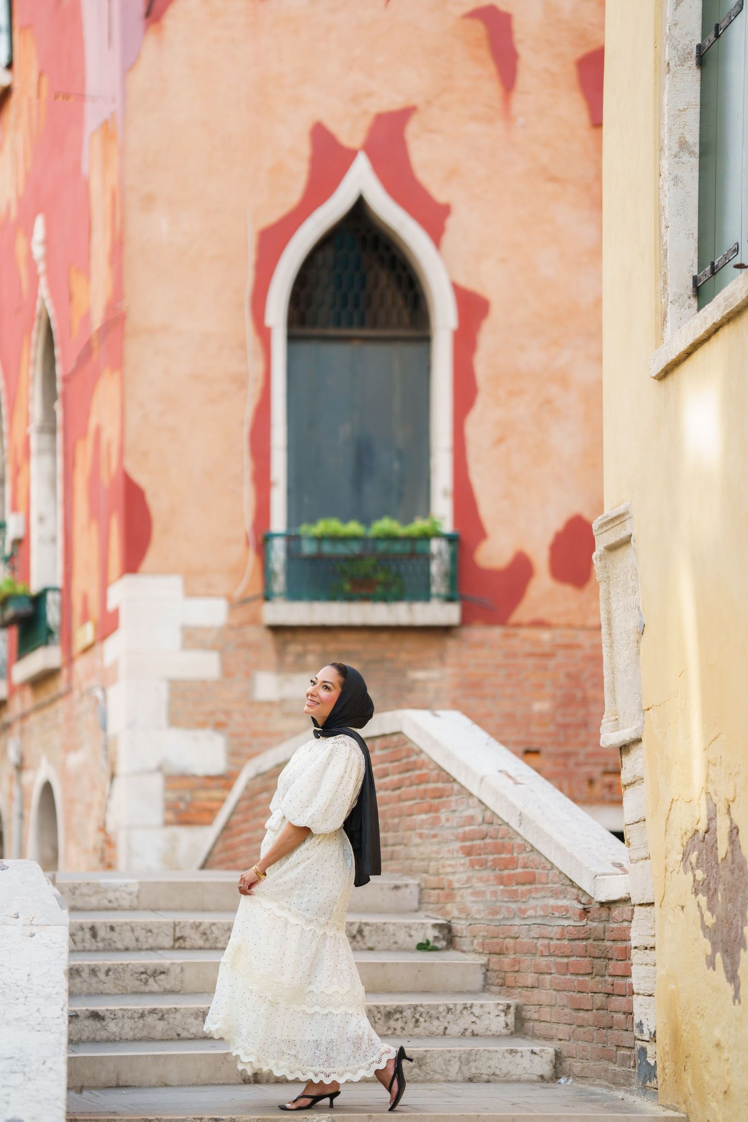 Muslim woman in white dress and hijab walking up brick steps in Venice, Italy.