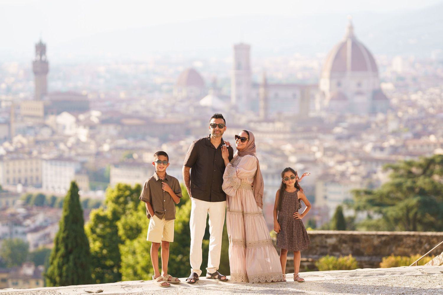 Family of four posing with Florence skyline, Duomo cathedral visible in background on sunny day.