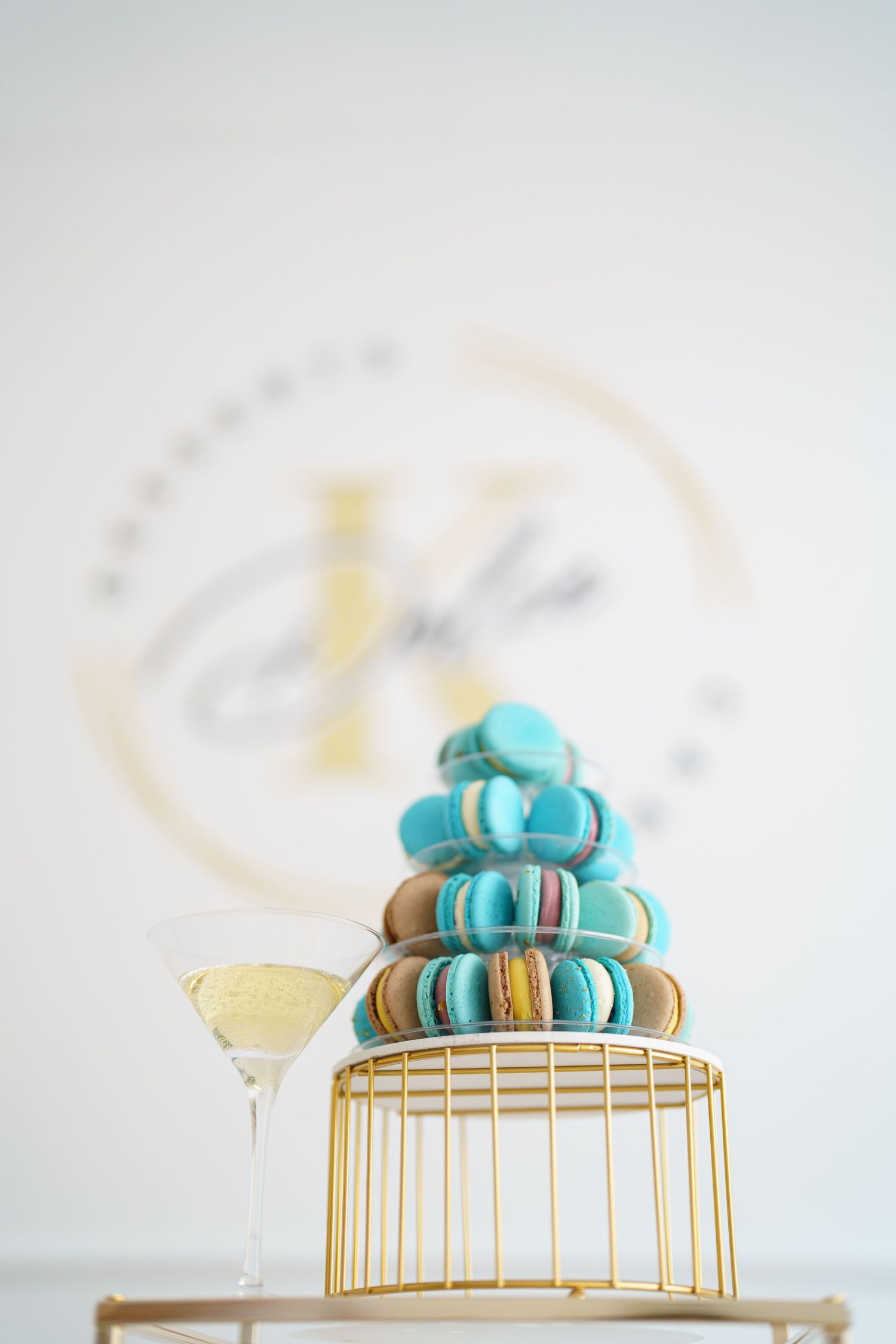Elegant macaron tower in blue and gold hues displayed on a golden birdcage stand beside a champagne glass.