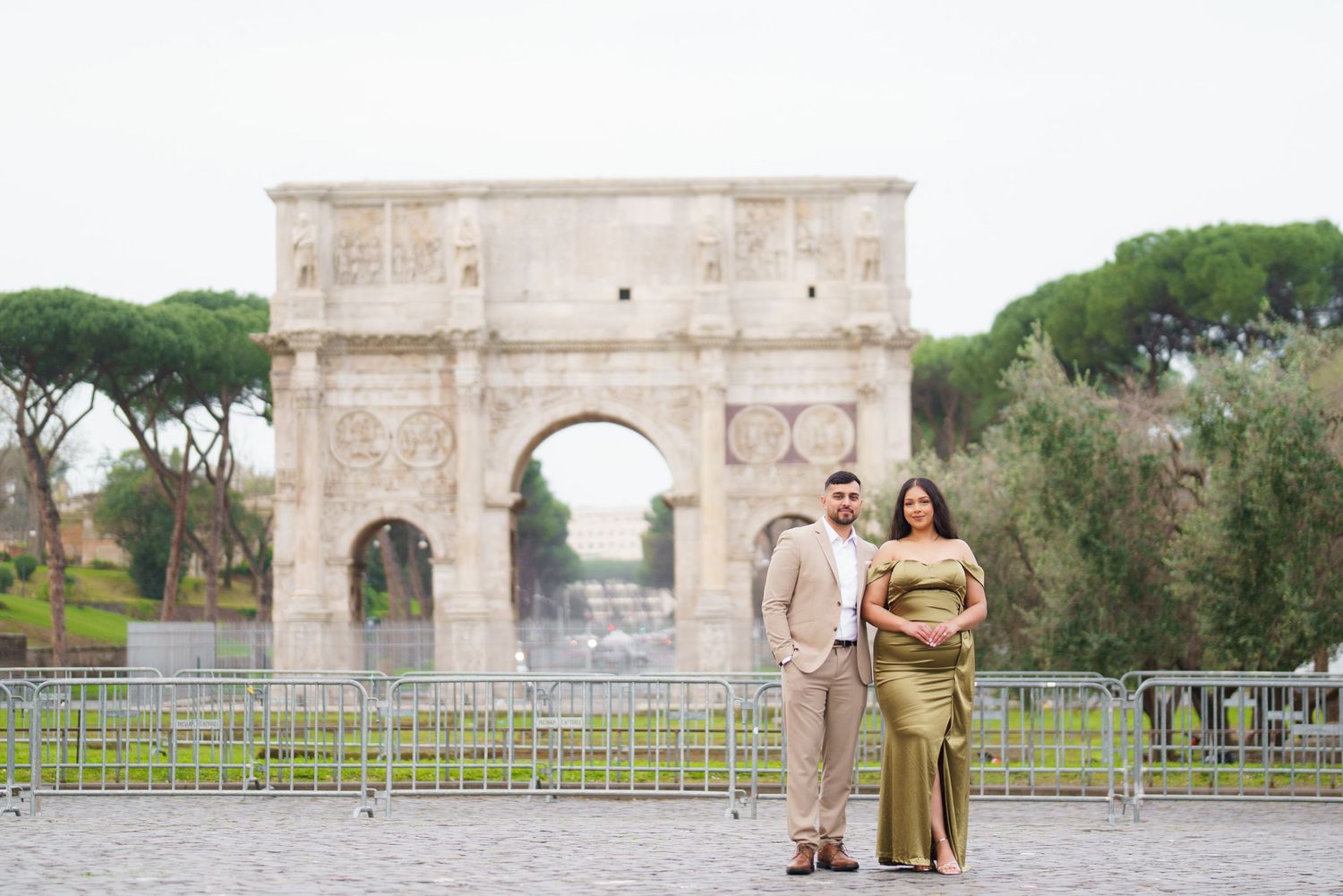 Couple posing in front of the Arch of Constantine in Rome, woman in gold dress, man in tan suit.