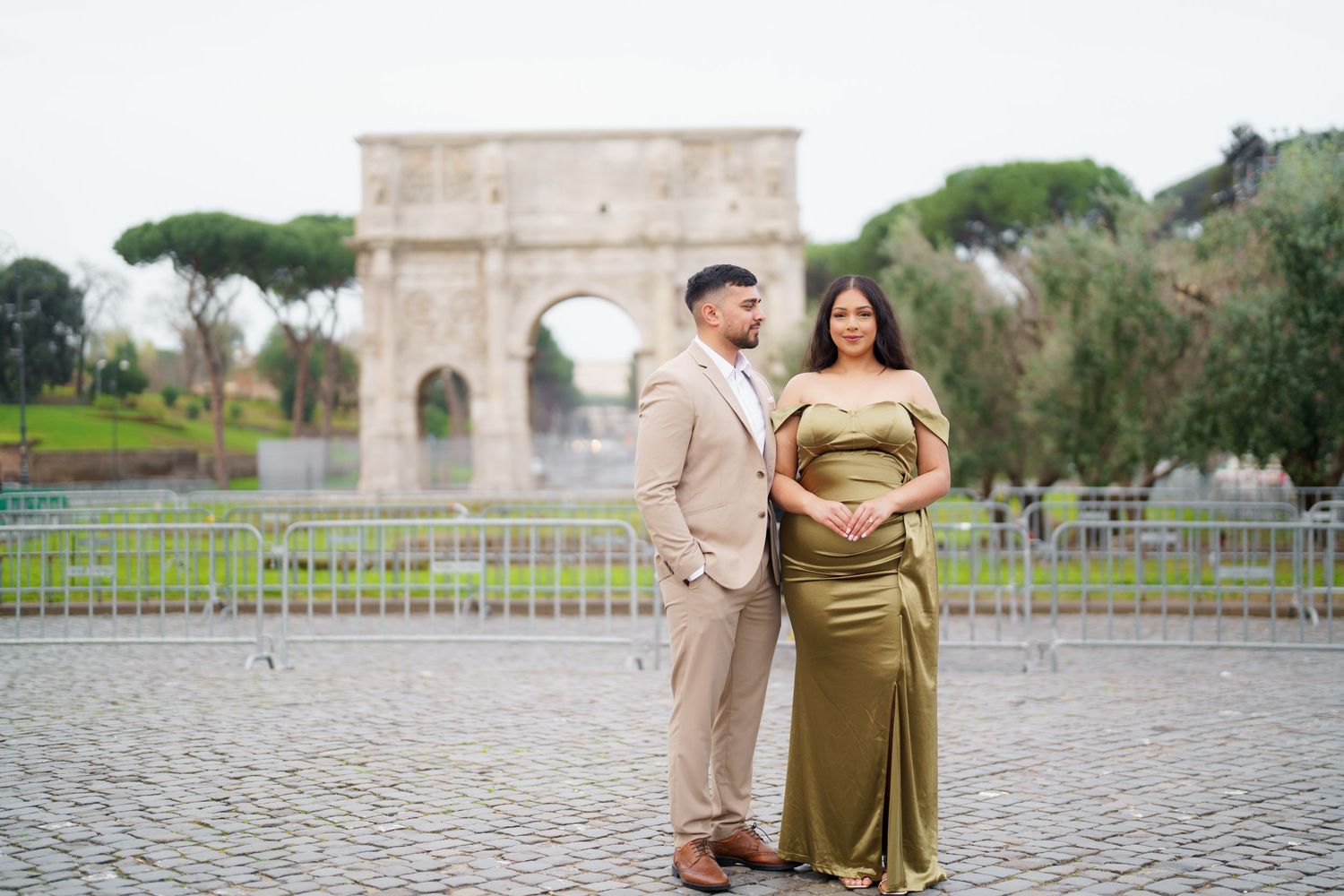 Couple in elegant attire posing before the Arch of Constantine in Rome, Italy.