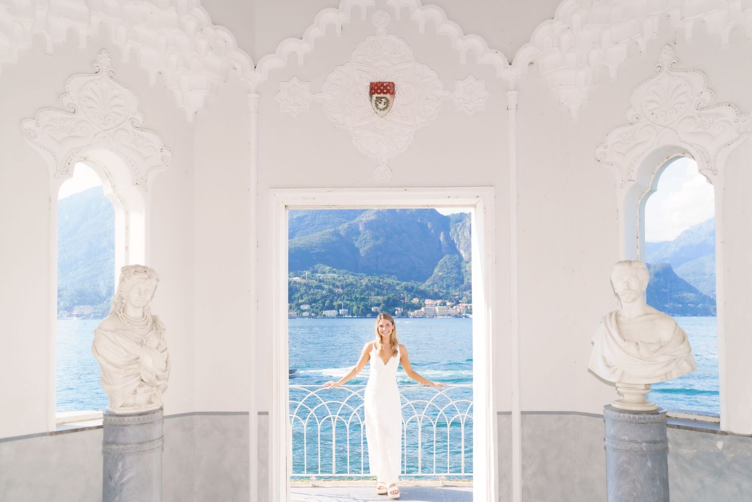 A series of scenic white-framed windows overlooking a tranquil lake with mountains in the background.