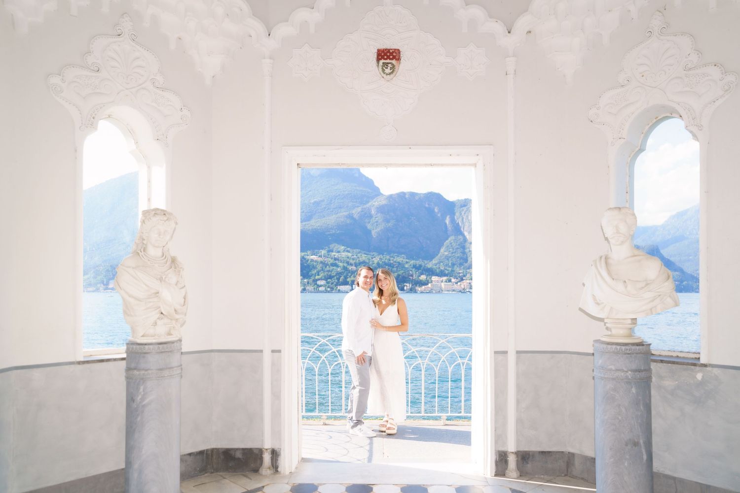 A panoramic view of a white columned terrace overlooking mountains and a lake in a scenic location.