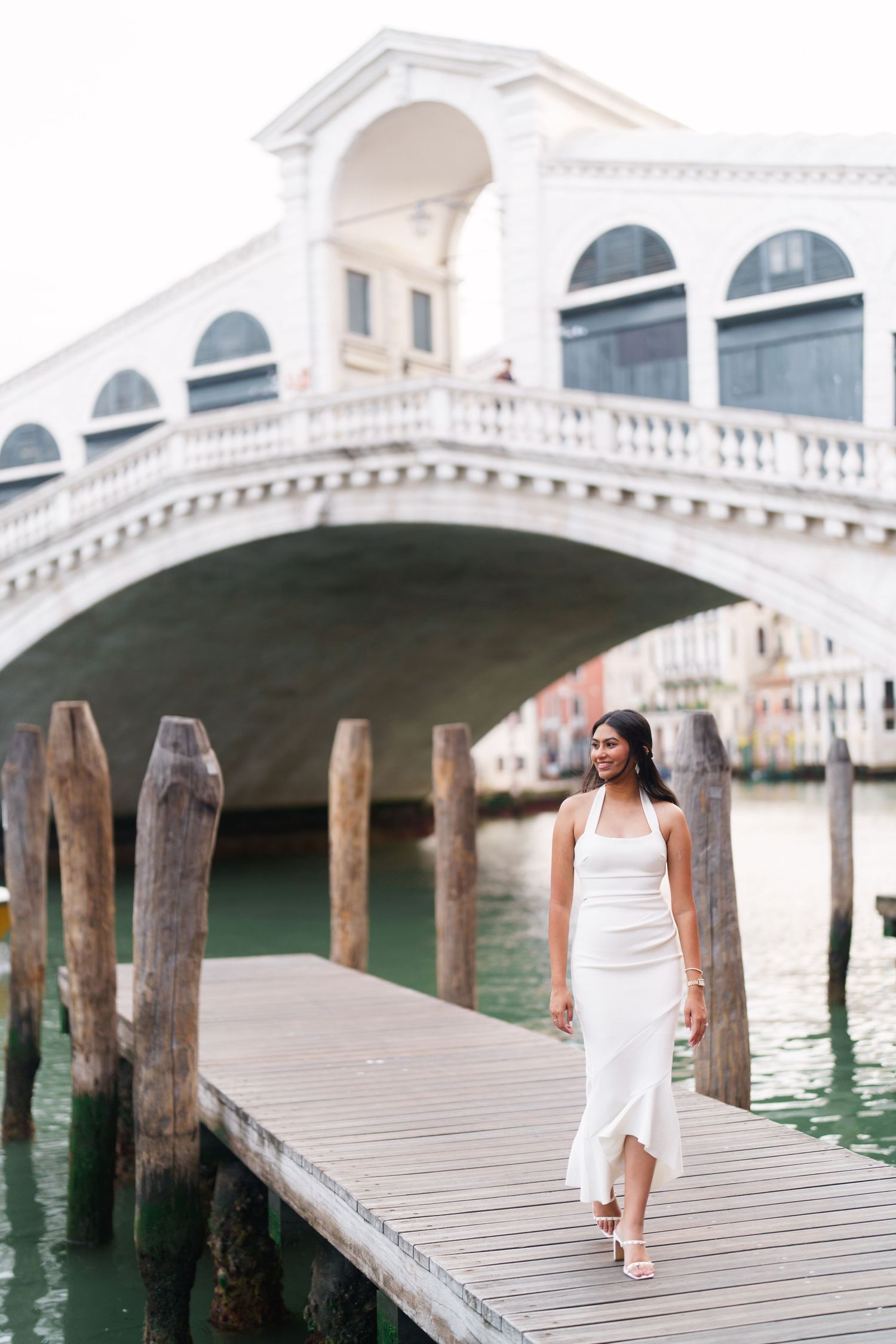 Scenic view of a wooden dock walkway along Venice's Grand Canal with the iconic Rialto Bridge in the background.