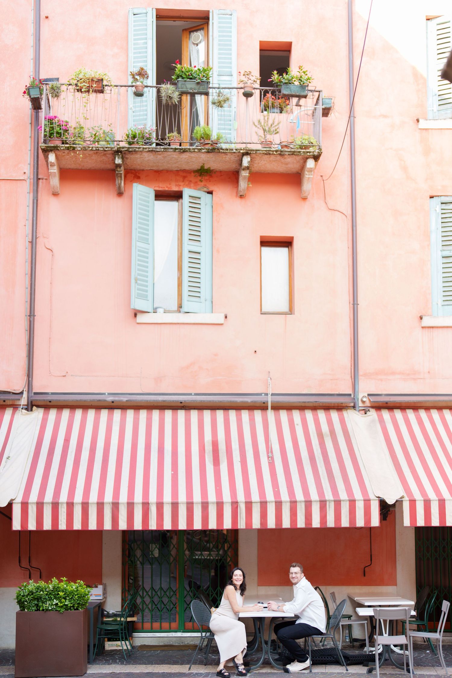 Pink building with blue shuttered windows and red and white striped awning on a European street.