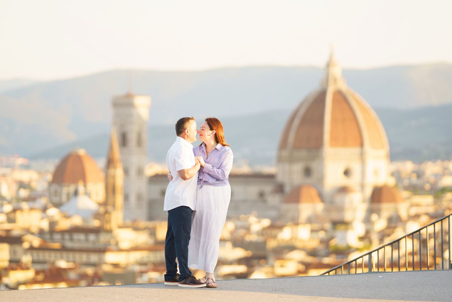 Two people in white outfits stand on a scenic overlook with Florence's iconic Duomo cathedral and cityscape in the background.