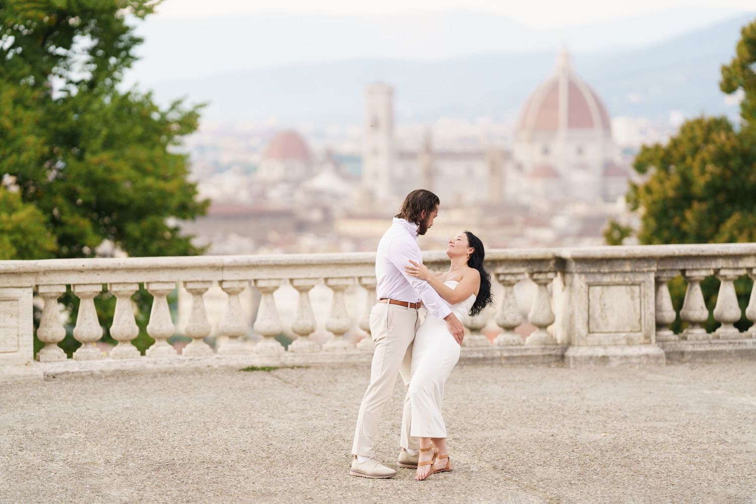 A romantic couple shares an intimate moment on a stone terrace overlooking Florence, Italy on a sunny day.