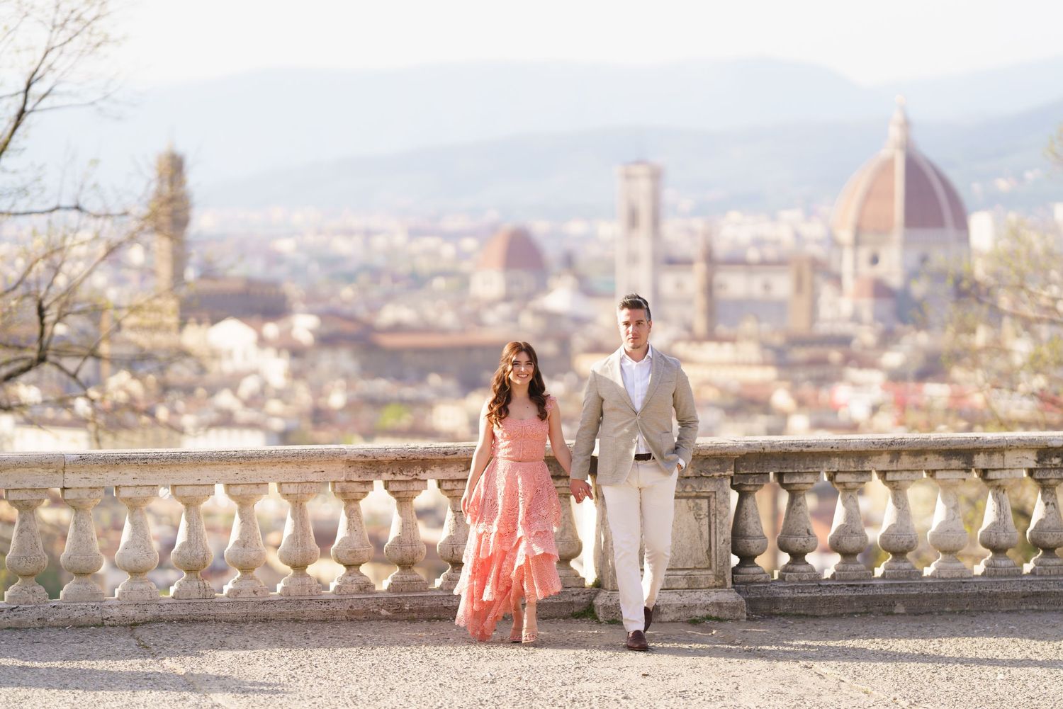 A couple strolls along a scenic terrace overlooking Florence's skyline with the iconic Duomo cathedral in the background.