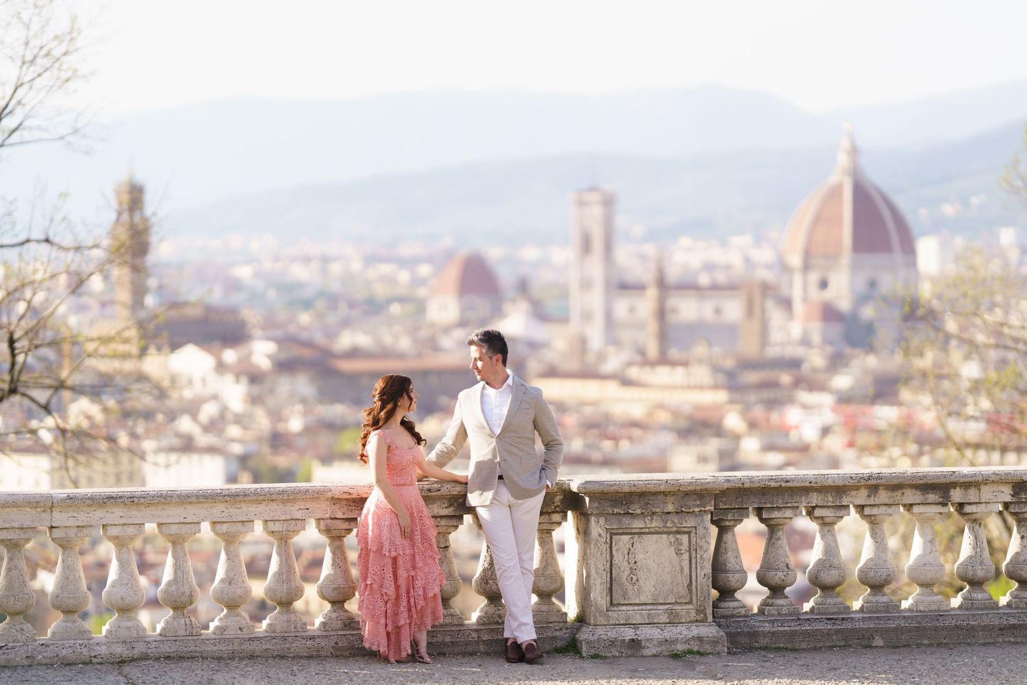 A couple stands at a scenic overlook with Florence's Duomo cathedral and cityscape visible in the background.