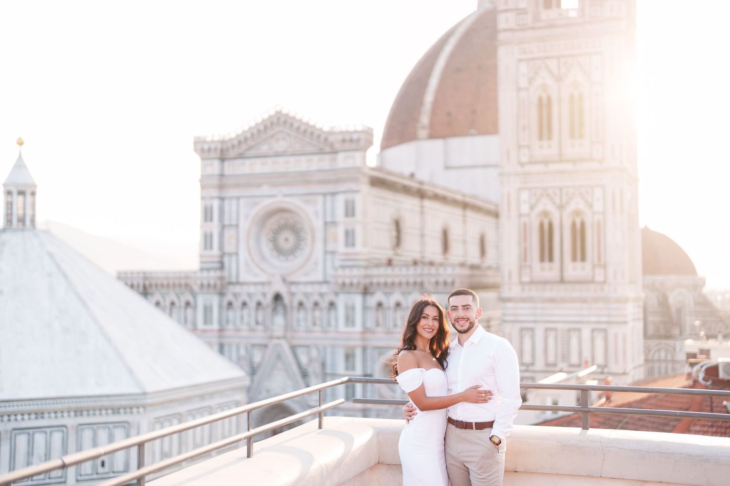 A couple embraces on a rooftop terrace overlooking Florence Cathedral and historic architecture during sunset.