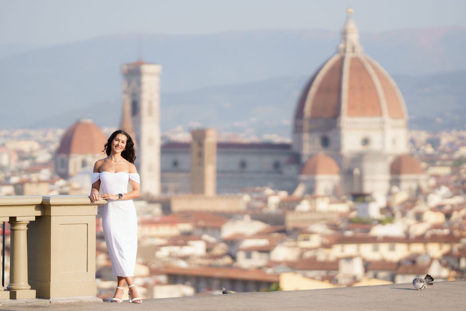 Panoramic cityscape of Florence, Italy showing the Duomo cathedral dome and bell towers against a bright sky.