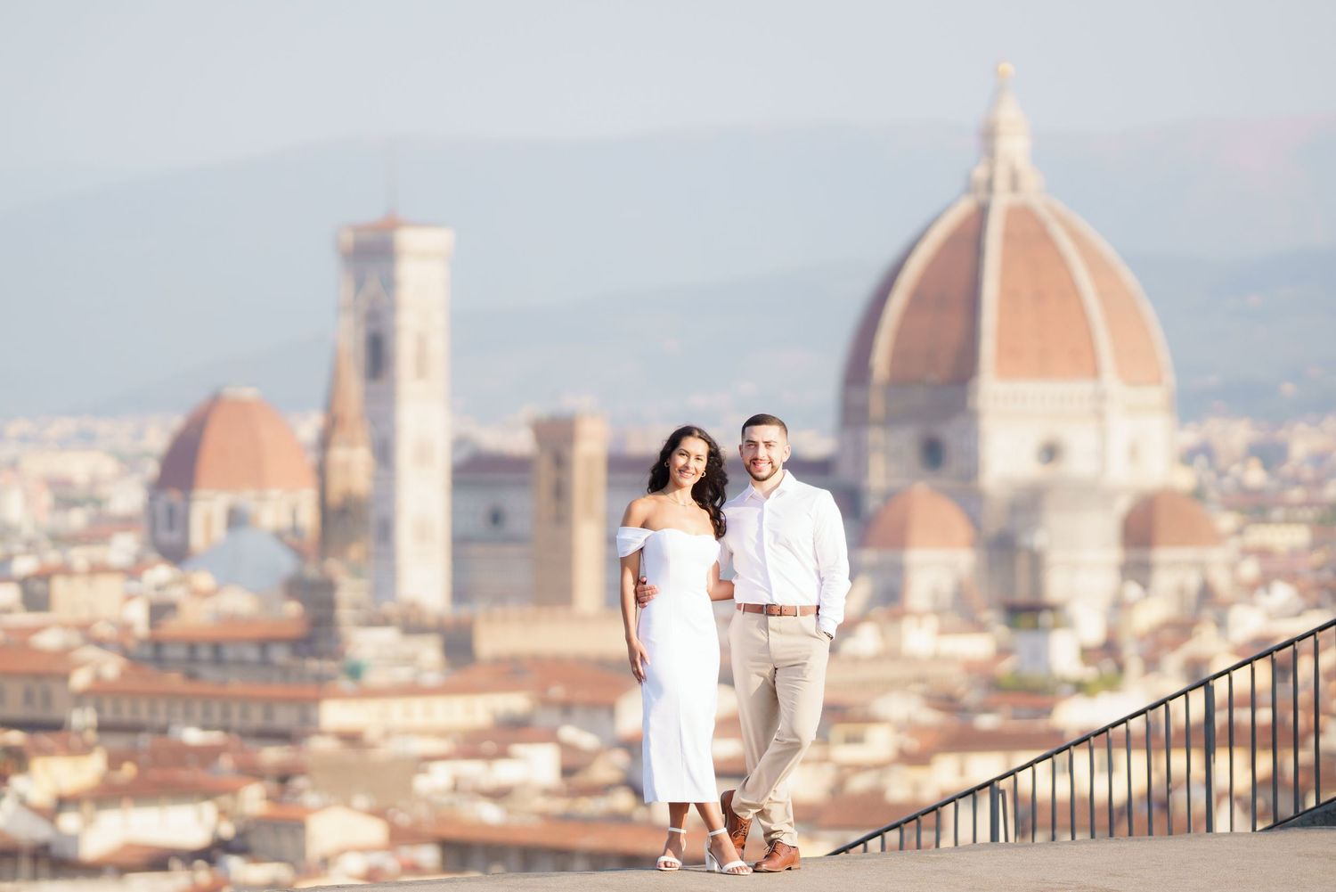 Couple walking along scenic viewpoint overlooking Florence with Duomo cathedral dome in background.