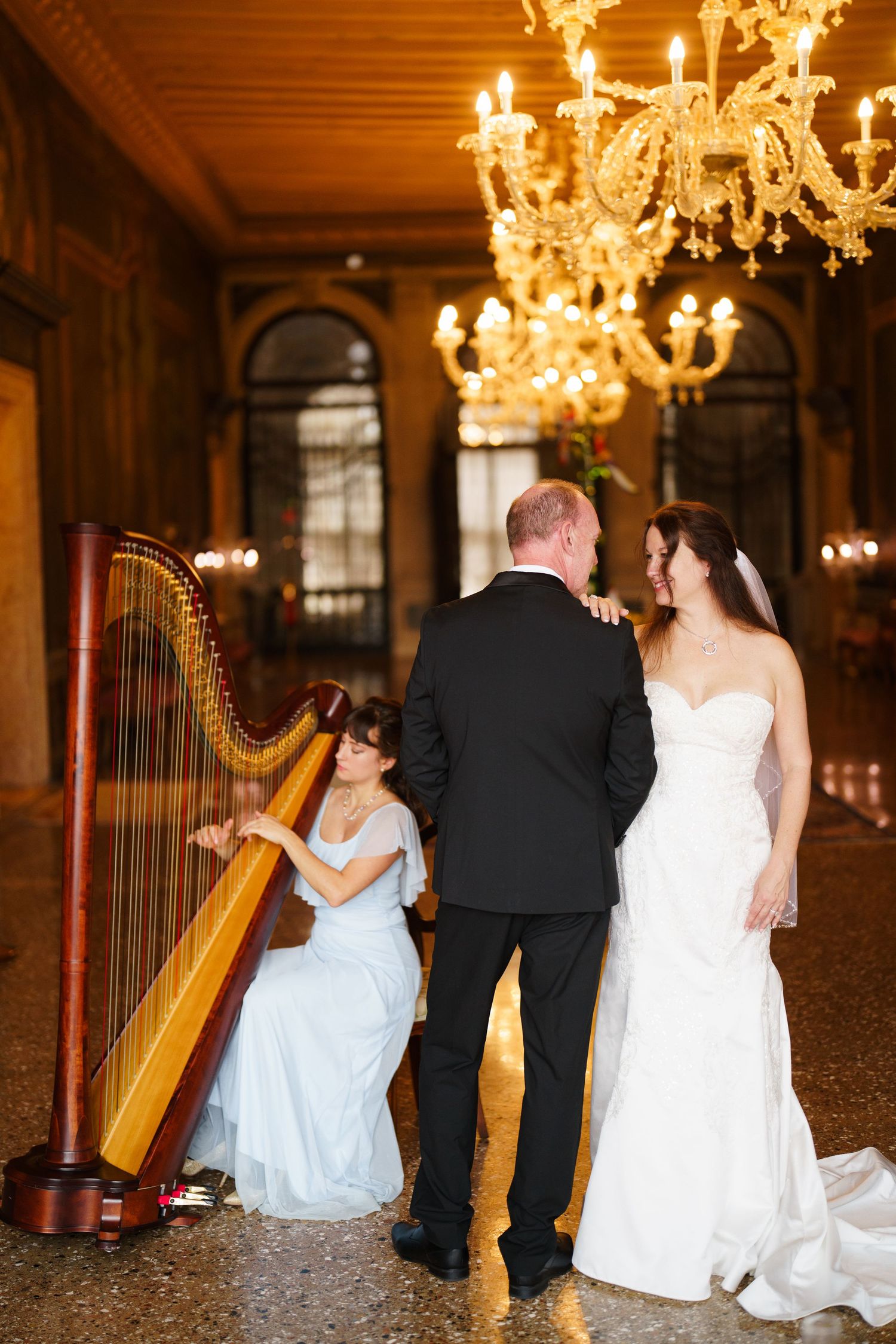 Elegant wedding reception scene with a golden harp and glowing chandeliers in a grand ballroom.
