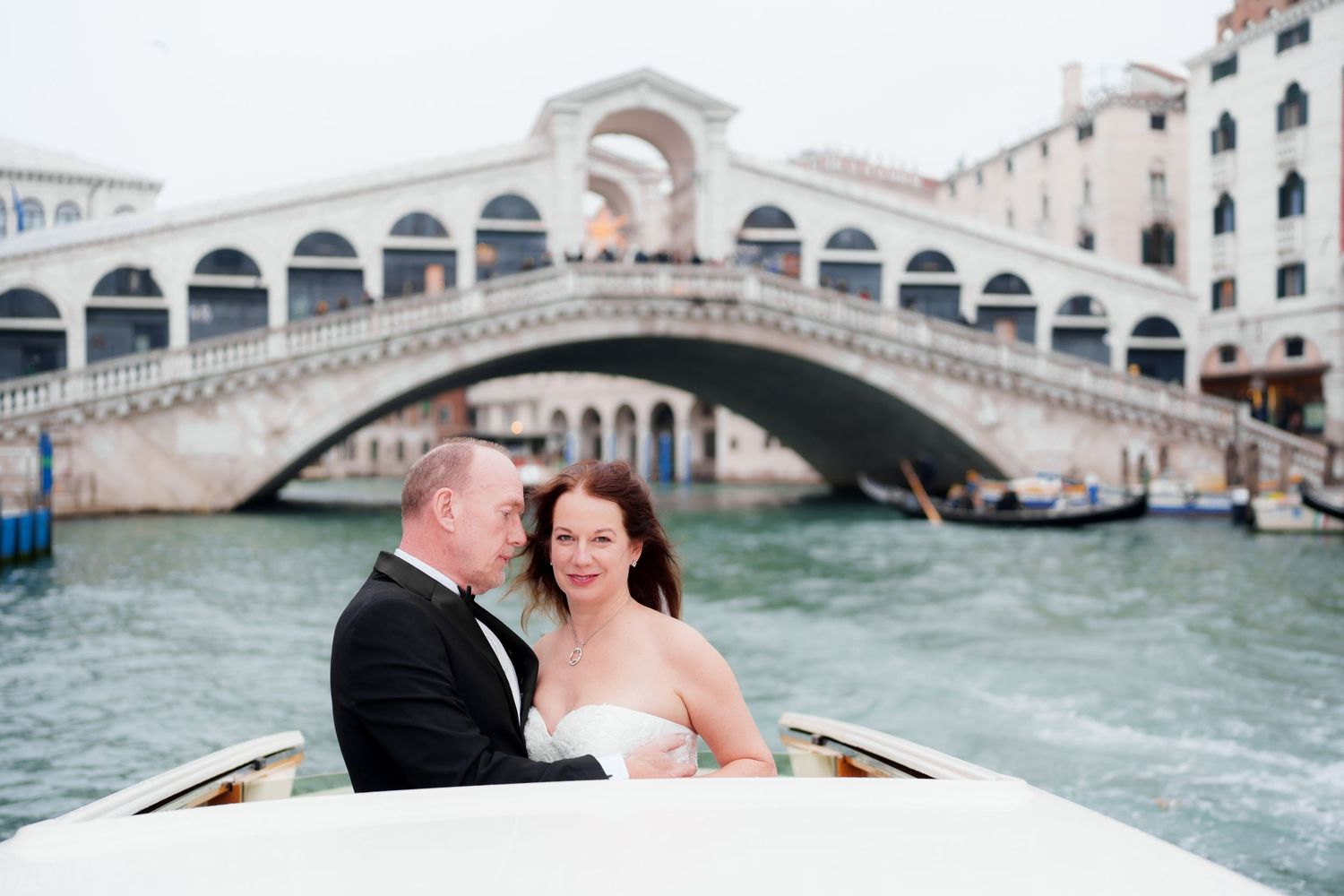Couple enjoying a romantic gondola ride through the scenic canals of Venice with the Rialto Bridge in the background.