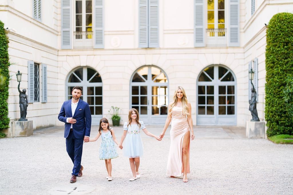 A family in coordinated blue and white outfits walks together in an elegant white courtyard.