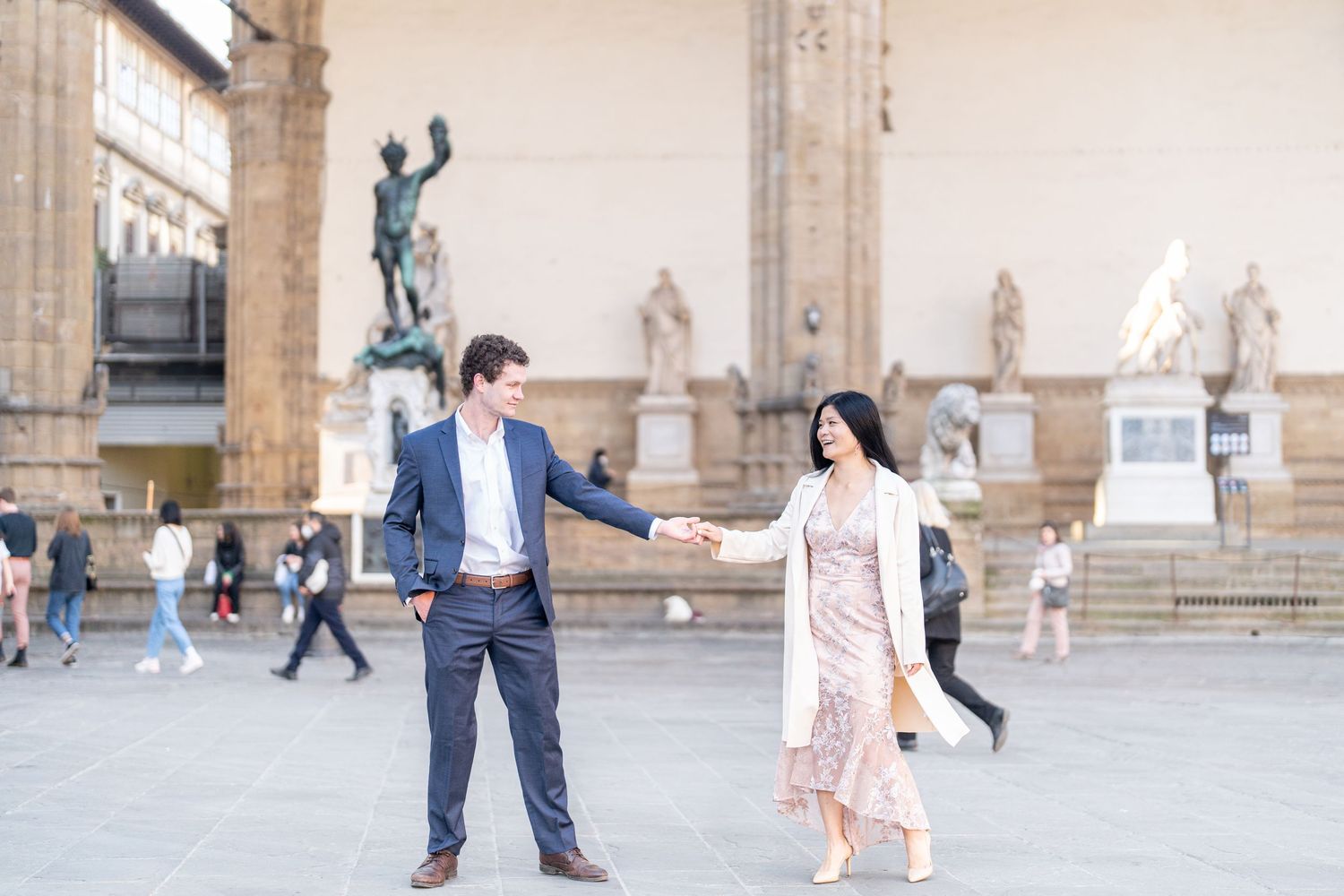 A couple holds hands and poses in front of historic statues at Piazza della Signoria in Florence, Italy.