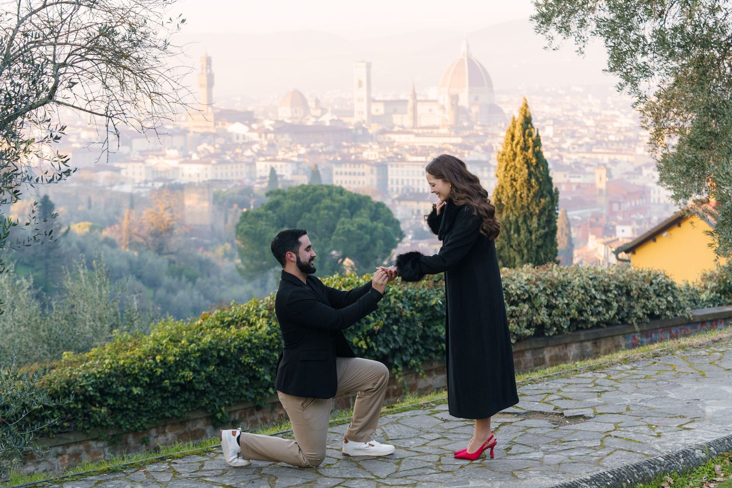A romantic proposal scene unfolds on a scenic overlook with a cityscape backdrop in the distance.